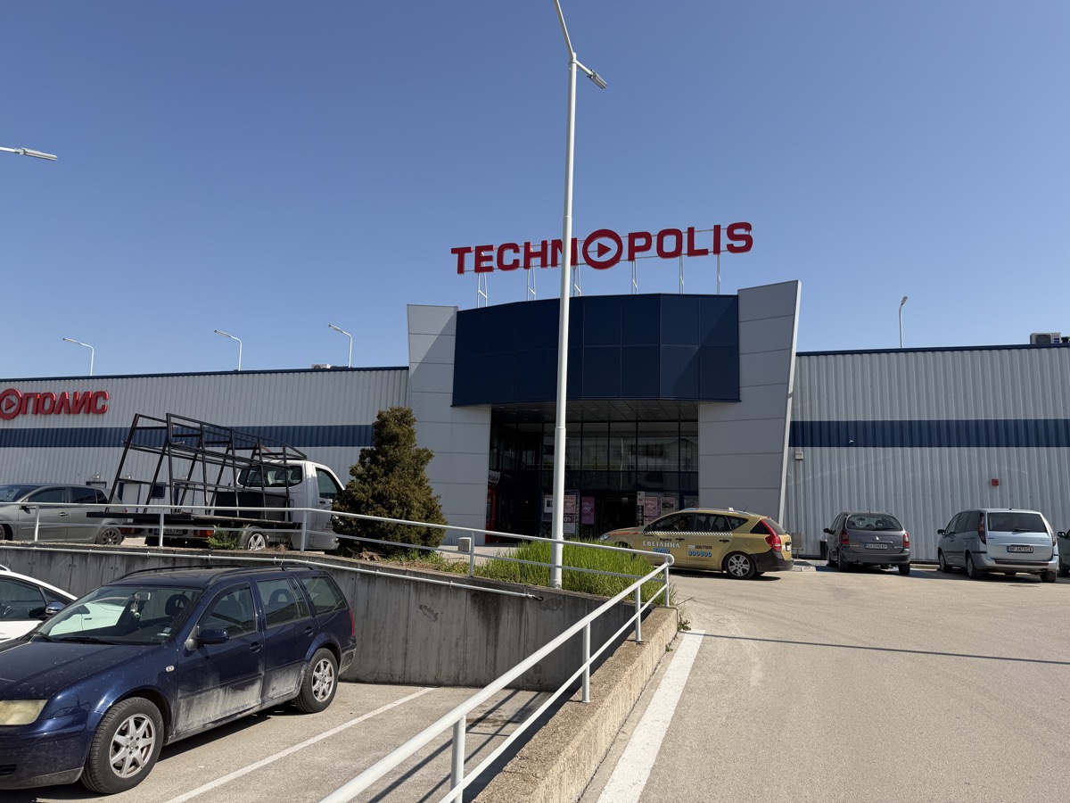 The TECHNOPOLIS electronics store — a large retail building with bold red signage, wind turbine in front, cars parked outside